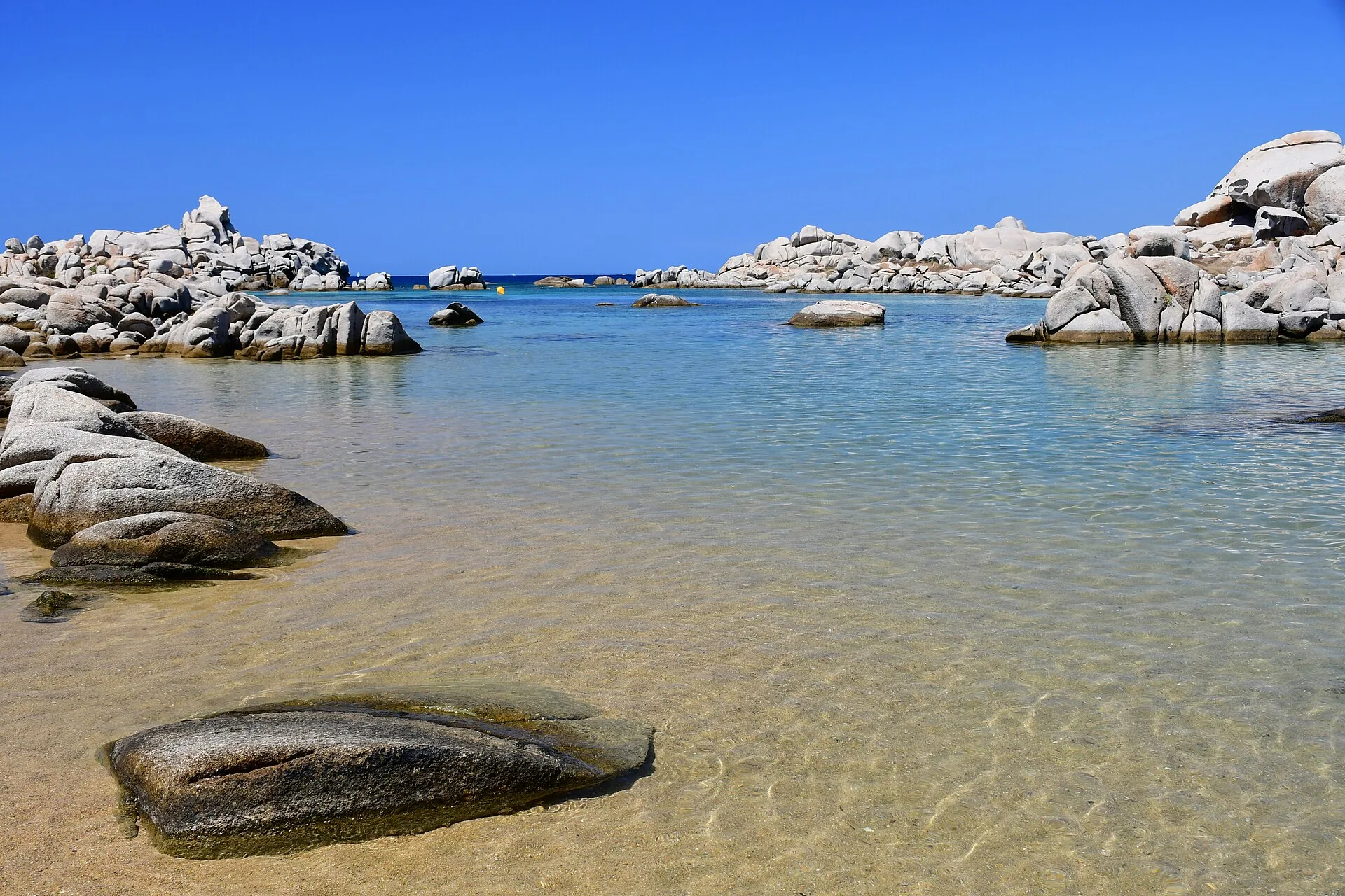 Crique de sable clair et d'eau turquoise bordée de rochers de granite blanc aux îles Lavezzi, sous un ciel bleu