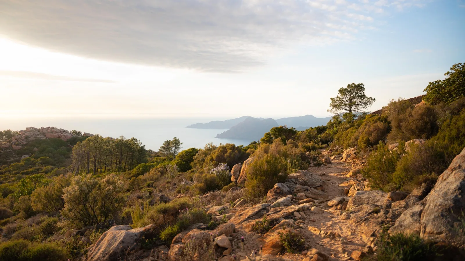 Randonneur seul sur un sentier de montagne corse avec sac à dos, vue sur les crêtes et le maquis